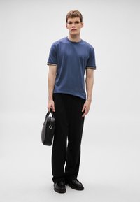 Kék, kerek nyakú, rövid ujjú póló, fekete nadrág és fekete táska. A póló ujjai csíkosak, kontrasztos színekben. Sima szövet textúra.