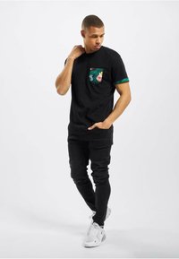 Fekete pamut póló virágmintás zsebből és zöld mandzsettából, fekete skinny farmerral és fehér tornacipővel párosítva.