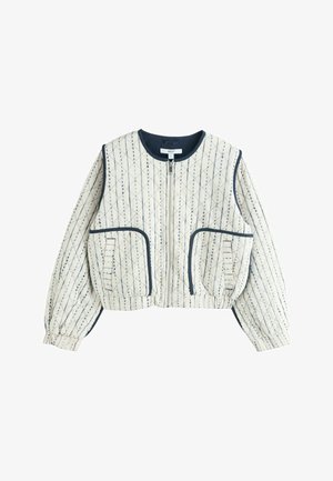 Krémová prošívaná bunda s tmavě modrým diamantovým prošíváním, předním zipem, dvěma velkými předními kapsami, elastickými manžetami a tmavě modrým lemováním na límci a kapsách.