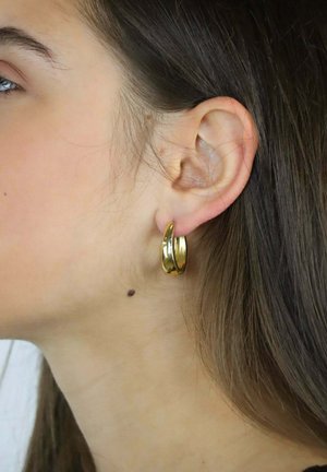 Orecchini a cerchio in oro con un design elegante e curvo. Superficie liscia e lucida e silhouette aperta che evidenziano la loro estetica minimalista.