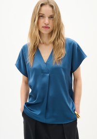 Bluză scurtă, albastră, cu mânecă scurtă și decolteu în V, având un finisaj texturat și croială lejeră, completată de o pereche de pantaloni negri și un inel cu accente aurii.