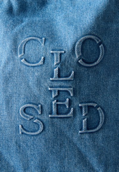 Μπλε υλικό τζιν με τη λέξη "ΚΛΕΙΣΤΟ" κεντημένη με μεγάλα, ανοιχτό μπλε γράμματα τοποθετημένα κάθετα και οριζόντια.