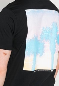 Černé bavlněné tričko s pastelovou grafikou palem a západu slunce na zádech, v designu s logem Levi's.