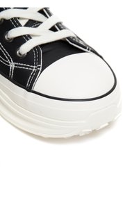 Czarne płócienne sneakersy z białą gumową czubką i podeszwą, z białymi sznurówkami i kontrastującymi białymi ściegami. Teksturowana podeszwa zapewniająca dobrą przyczepność.