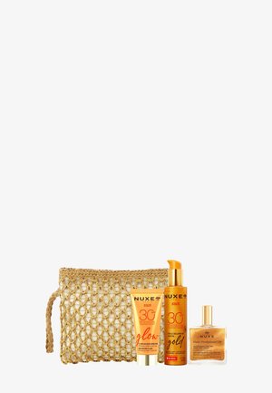 Tres productos de cuidado de la piel Nuxe Sun con SPF 30 y un bolso cosmético de tono dorado tejido sobre un fondo blanco.