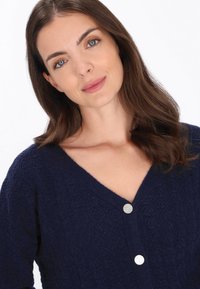 Marineblauwe cardigan met een textuurpatroon, diepe V-hals en twee decoratieve knopen aan de voorkant. Zacht materiaal met een comfortabele pasvorm.