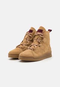 Bottes hautes en suède beige avec des accents bordeaux. Caractéristiques : lacets à motifs et semelle en caoutchouc texturée pour une meilleure adhérence. Détails sur le côté.