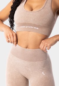 Bēša sporta krūšturis un augstās jostasvietas legingi ar ribotām akcentiem. Krūšturim ir logo uz joslas. Mīksta, teksturēta auduma.