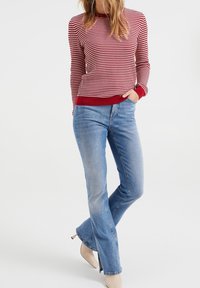 Pull en tricot rayé rouge et blanc avec ourlet côtelé, associé à un jean évasé bleu clair et des talons beiges. Design simple, coupe décontractée.