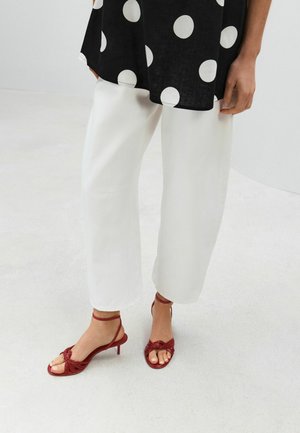 Lower body of a person wearing white wide-leg pants, a black top with large white polka dots, and red strappy heeled sandals.