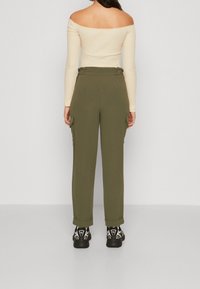 Olivově zelené cargo kalhoty s bočními kapsami, spárované s béžovým topem bez ramínek a černými teniskami s bílými detaily.