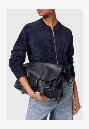 Mustat nahkakäsilaukku, jossa on teksturoitu pinta, taitettu yläosa ja kaksinkertaiset kahvat. Yhdistettynä tummansiniseen pörröiseen neuleeseen ja vaaleansiniin farkkuihin.