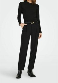 Svart långärmad topp med spetsdetaljer, kombinerat med höga svarta byxor med veck och ett svart bälte med en guldbuckle. Svarta ankelskor.