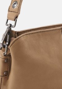 Sac en cuir tan avec une texture lisse, présentant un crochet à pression en métal et des clous décoratifs, ouverture supérieure partiellement visible et anse.