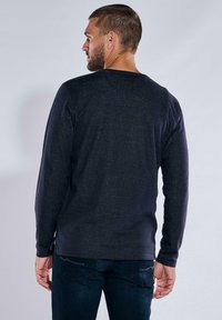 Dunkelblaues Langarmshirt mit Rundhalsausschnitt, strukturierter Oberfläche und seitlichen Schlitzen am Saum, kombiniert mit dunklen Jeans.