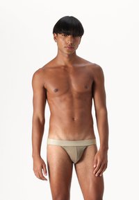 Beige tangatrusser med mjukt elastiskt midjeband, minimalistisk design och slät textur. Åtsittande och låg skärning.