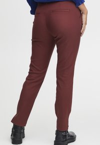 Burgundské slim-fit kalhoty s hladkým povrchem, s kapsami na zadní straně a zúženým střihem nohavic. Kombinovány s černými kotníkovými botami.
