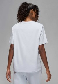T-shirt bianco in cotone con maniche corte e vestibilità rilassata, con scollatura a girocollo e trama liscia, mostrato da dietro.