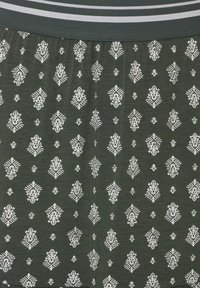 Grüner Stoff mit weißem geometrischem Muster, einer strukturierten Oberfläche und einem kontrastierenden, gestreiften Taillenbund.