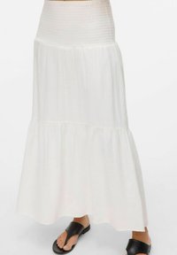 Jupe maxi blanche en tissu léger, avec une taille haute froncée et un design à volants. Associée à des sandales plates noires.