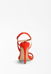 Rød ruskinds højhælet sandal med åben bag, tynd ankelrem og spids tå. Hælhøjden er ca. 10 cm.