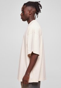 Beige, oversized pamut póló. Kerek nyakkal, rövid ujjakkal és laza fazonnal rendelkezik, sima textúrájú, látható minták nélkül.