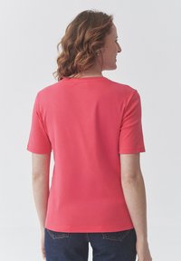 Kratký rukáv korálové tričko s kulatým výstřihem, vyrobené z jemné tkaniny. Má hladký design s jemnou texturou a přiléhavý střih.