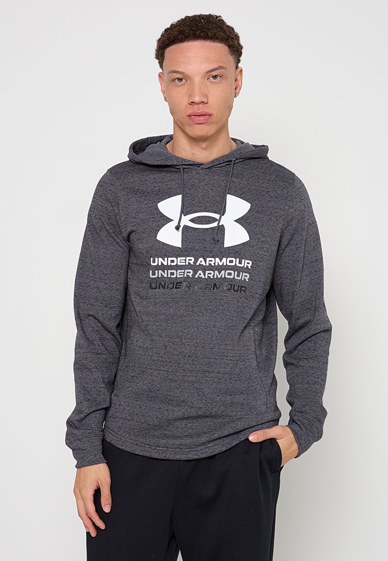 Sudadera gris de tejido texturizado, con un gran logo blanco de Under Armour y capucha con cordones. Modelo lleva pantalones negros.