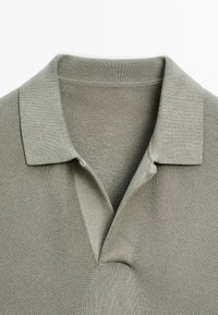 Pikétröja i en dämpad grön nyans, med en texturerad stickad tyg, tvåknapplås och en mjuk krage med subtil ribbning.