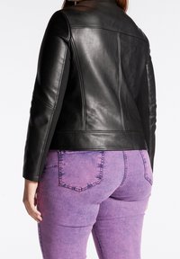Černá kožená bunda s přizpůsobeným střihem, včetně zkráceného provedení a hladké textury. Nositá přes fialové džíny.