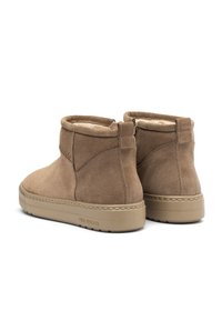 Ein Paar tanfarbene Wildleder-Stiefeletten mit Fleecefutter und beigen Gummisohlen, von hinten auf einem weißen Hintergrund betrachtet.