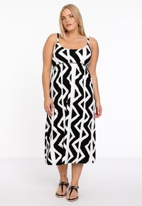 Robe midi noire et blanche avec un motif en zigzag, bretelles ajustables et taille élastique, associée à des sandales plates.