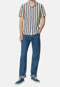 Camicia a maniche corte con colletto, a righe verticali blu, bordeaux e crema, abbinata a jeans in denim blu e sneakers blu.