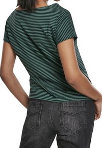 Zelené a černé pruhované tričko s kulatým výstřihem a krátkými rukávy, spárované s tmavě šedými džíny z denimu, které mají zadní kapsy a mírné vyblednutí.