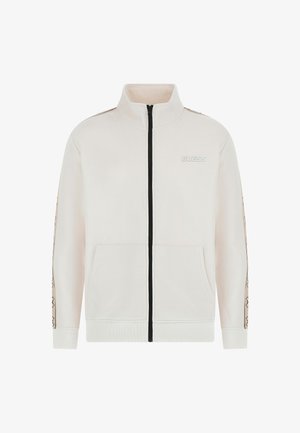 Veste zippée beige clair avec col haut, fermeture éclair noire et logo. Comprend des poches latérales et des accents à motifs contrastés sur les manches.
