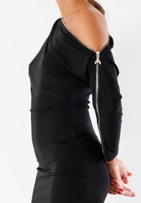 Abito nero con una manica scoperta, caratterizzato da una zip argentata sul braccio. Materiale liscio e elasticizzato con una silhouette aderente.