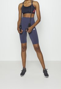 Granatowe, wysokie spodenki rowerowe o miękkiej fakturze i dopasowanym kroju, zestawione z czarnym biustonoszem sportowym z czerwonymi akcentami oraz skakanką.