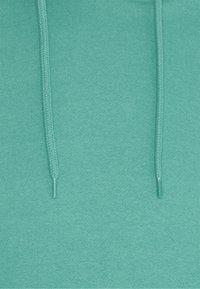 Felpa con cappuccio di un uniforme colore turchese, realizzata in morbido tessuto a maglia con due cordini intrecciati e una texture liscia.