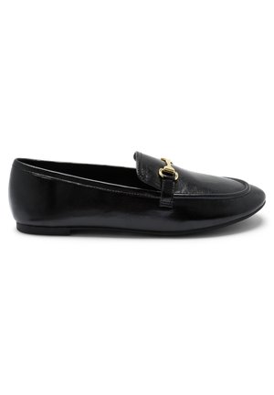Mocassin en cuir noir avec un détail de boucle en métal doré sur le dessus, semelle plate et bout arrondi, vu de profil sur fond blanc.