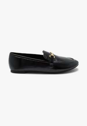 Mocassin en cuir noir avec un détail de boucle en métal doré sur le dessus, semelle plate et bout arrondi, vu de profil sur fond blanc.