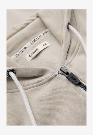 Sweat à capuche beige zippé avec cordons blancs, doublure en polaire, et étiquette « ombre cotton line » à l'intérieur du col, taille medium.