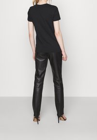 Camiseta negra ajustada con cuello redondo, combinada con pantalones de cuero negro de cintura alta y zapatos de tacón. Textura suave en toda la prenda.