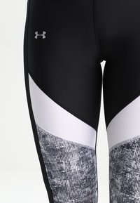 Svart och vita sportleggings med ett geometriskt mönster, slät textur och en logotyp på höftområdet.