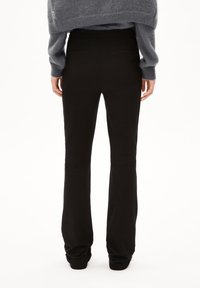 Černé rozšířené kalhoty s hladkou texturou, středně vysokým pasem, dvěma zadními kapsami a přiléhavým střihem od pasu dolů.