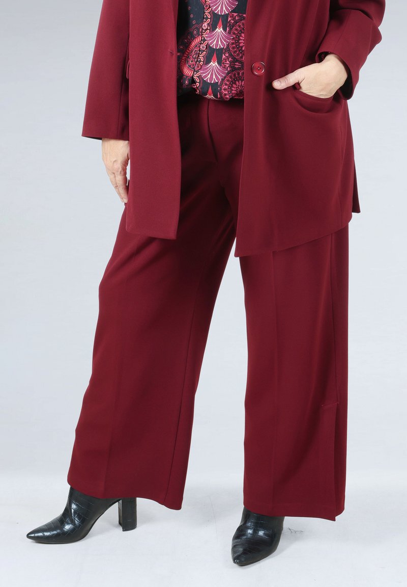 Burgundy tailored suit featuring wide-leg trousers and a long blazer. Black heeled shoes with a pointed toe and textured design.