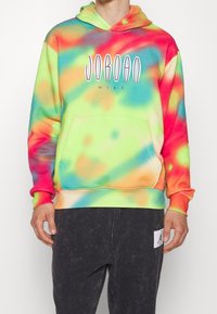 Person wearing a multicolored tie-dye Jordan Nike hoodie and black pants with a Jordan logo patch on the left thigh.