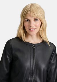 Svart läderjacka med rund hals och framdragskedja, som har ett runt draghandtag och subtila vertikala sömmar.