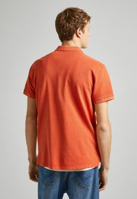 Krátký rukáv oranžová polo tričko vyrobené z bavlny, s klasickým límcem a rovním lemem, v kombinaci s modrými denimovými džíny.