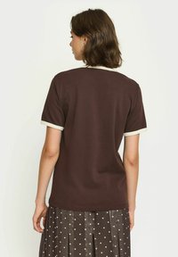 Brun kortærmet t-shirt med en cremefarvet ribbet halsudskæring, glat tekstur og en afslappet pasform, parret med en polka dot nederdel.