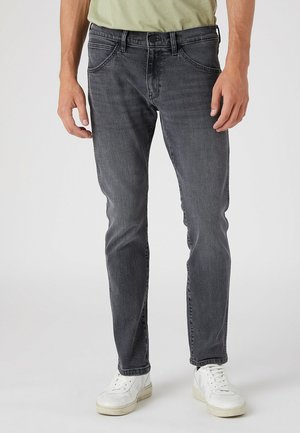 Jeans in denim grigio con vestibilità slim, leggermente sbiaditi, design a cinque tasche e chiusura con bottone in metallo, indossati con sneakers bianche.